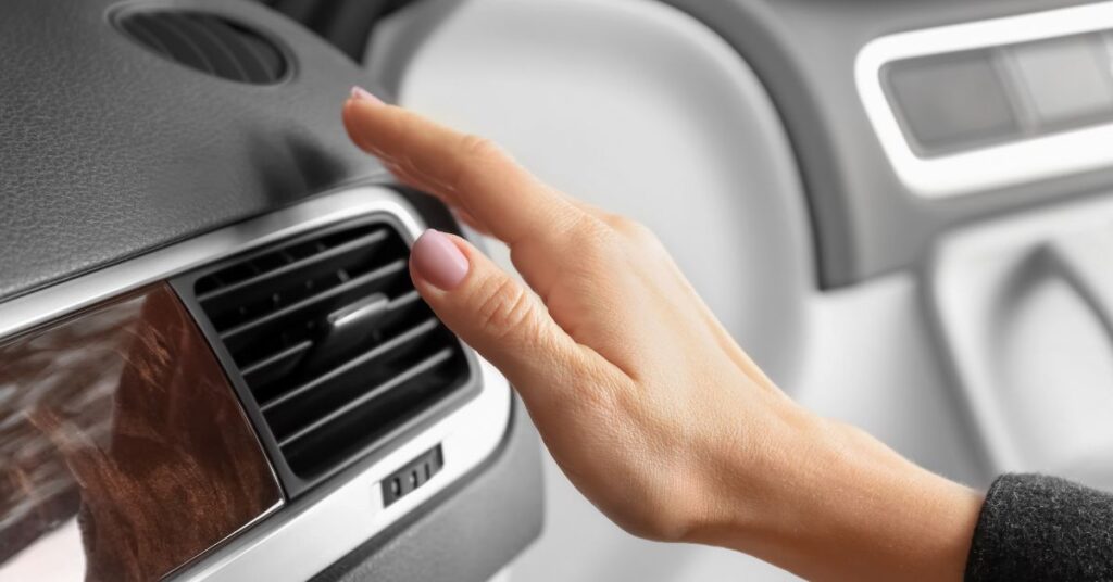 Hand adjusting car air conditioning vent on dashboard